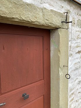 Die Tür gehört zu einer Synagoge. Der Türpfosten ist aus Stein. Auf dem Pfosten ist ein schräger Abdruck. Hier hing früher eine Mesusa.