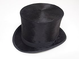 Der Hut ist schwarz. Er hat die Form eines Zylinders.
