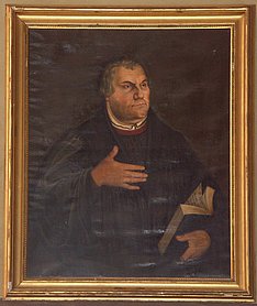 Bruststück Martin Luthers im gesetzten Alter, gekleidet mit schwarzer Schaube, in der linken Hand eine aufgeschlagene Bibel haltend, die rechte Hand erhoben