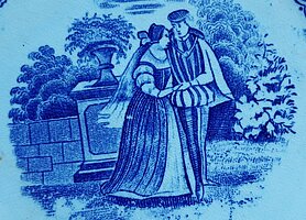 Auf dem Teller sind zwei Personen. Eine Frau und ein Mann. Sie halten sich an den Händen. Sie stehen in einem Park. Hinter ihnen ist ein Podest mit Blumenvase.