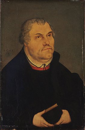 Bruststück Martin Luthers im gesetzten Alter, gekleidet in eine schwarze Schaube, mit beiden Händen ein Buch haltend