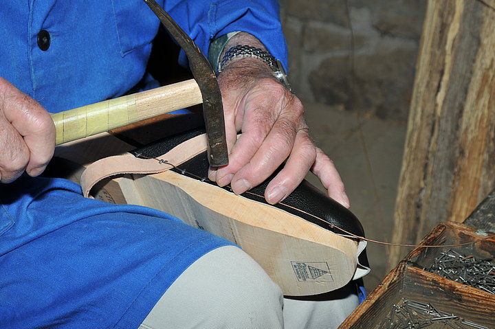 Ein Mann befestigt mit Nagel und Hammer Leder an eine Holzschuhsohle